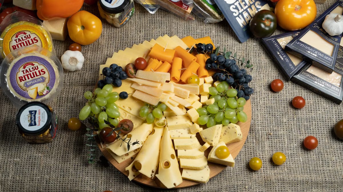 Aesthetic cheese platter with fresh grapes and vegetables on burlap background, ready for serving.
